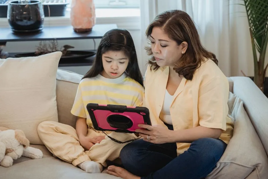 A parent and child sitting on a couch looking at a tablet together